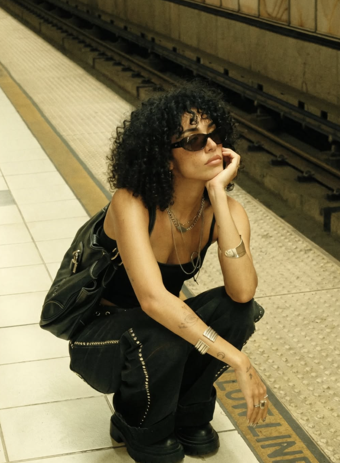 Layla Rey crouched on a subway platform in all black with silver cuffs